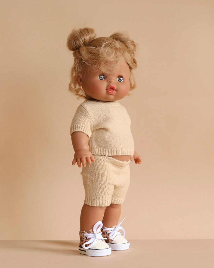 The Minikane Standing Doll (14") - Louisa with Clothing features light skin, curly blonde pigtails, and blue eyes. She stands against a beige background wearing an anatomically correct beige knit outfit and white sneakers with animal print, made in Spain.