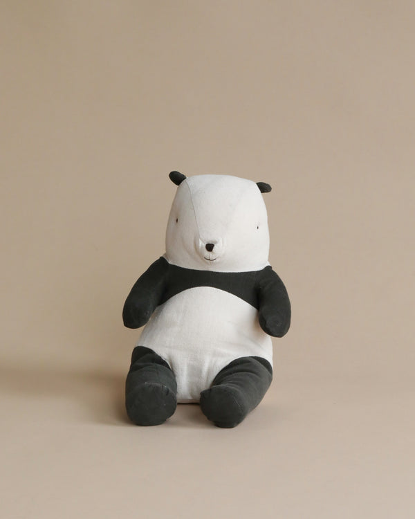 A plush toy of a Maileg Panda Stuffed Animal with a white face and body, and black ears, arms, and legs, sitting against a beige background.