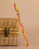 A clear resin wand with orange, yellow, and red accents and silver stars rests against a closed Easter Basket Gift Set with a metal clasp, all set on a beige background.