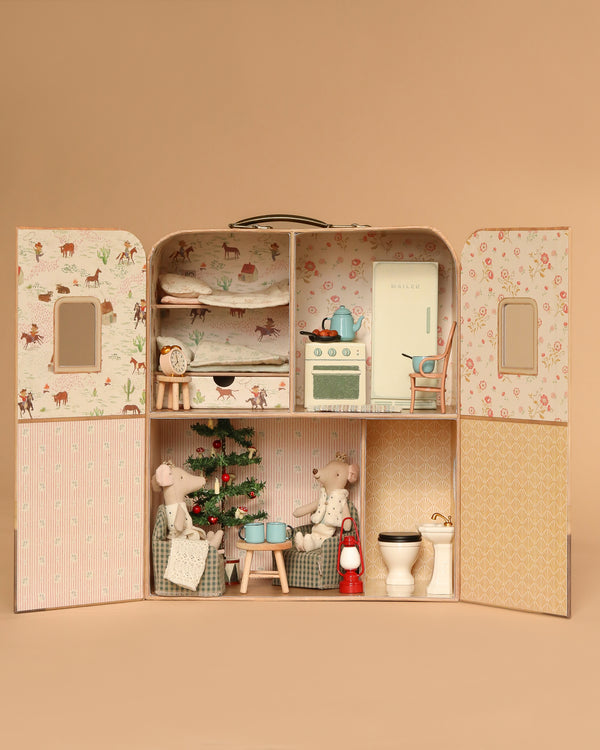 The Maileg Fully Furnished Christmas Suitcasa with Royal Twins features pastel rooms, a kitchen, living area, and bedroom. Royal Twin mice sit by the Christmas tree and kitchen furniture, with household items neatly arranged throughout.