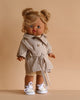 The Minikane Standing Doll (14") - Louisa with Clothing features a blonde, blue-eyed doll in a beige trench coat, shorts, and white sneakers with patterned socks, posed stylishly against a plain beige background.