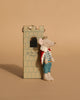 A Maileg Queen Mouse in a crown, red cape, blue pants, and floral shirt rests by the Maileg Royal Tower Set featuring a window and "Let the story begin" inscribed on it.