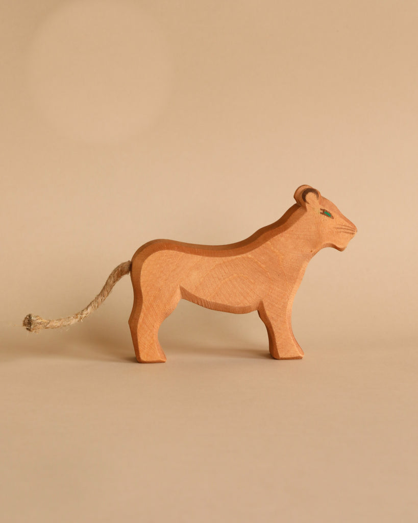 A small, carved Ostheimer Female Lion with simple detailing stands on a neutral beige background. Handcrafted from sustainably sourced materials, the lion has a short rope tail and minimal painted features to indicate the eyes and facial expression, reminiscent of Ostheimer toys.