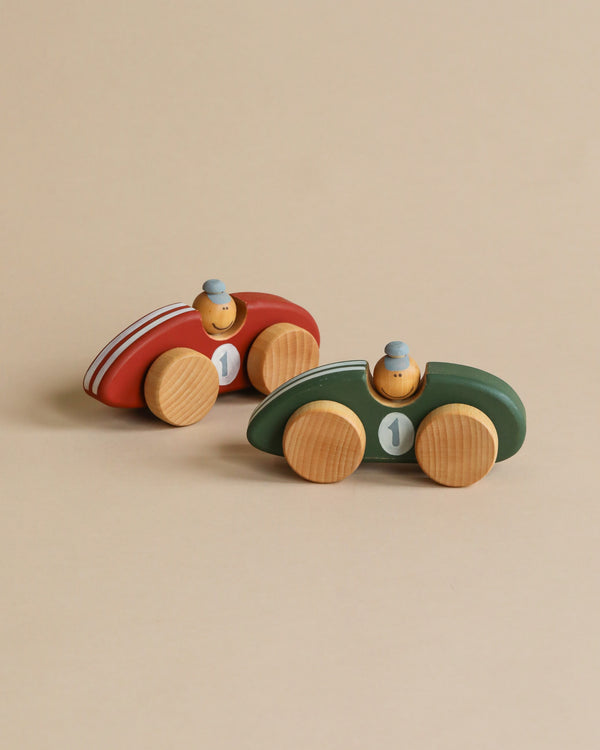 Two handcrafted wooden toy race cars made from sustainably harvested birch wood sit on a light beige background. One car is red with white stripes and the number "1," while the other is green with the same number. Both Handmade Wooden Toy Race Cars feature small wooden driver figures wearing blue hats.