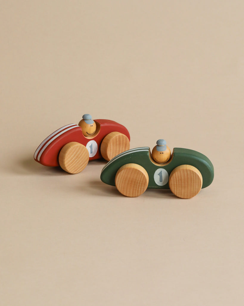 Two handcrafted wooden toy race cars made from sustainably harvested birch wood sit on a light beige background. One car is red with white stripes and the number "1," while the other is green with the same number. Both Handmade Wooden Toy Race Cars feature small wooden driver figures wearing blue hats.