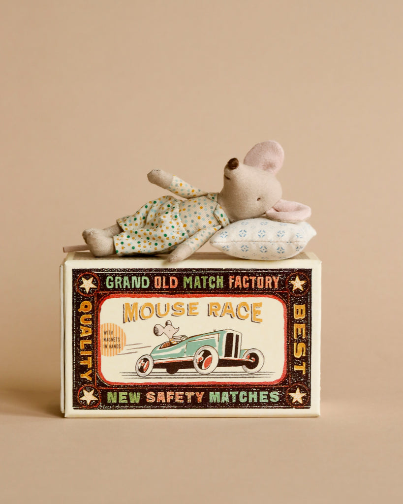 A Maileg Little Brother, Mouse In Matchbox toy with a patterned outfit sitting on a colorful vintage matchbox that reads "Grand Old Match Factory Mouse Race - Quality - Best - New Safety Matches.
