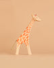 The Ostheimer Handmade Wooden Giraffe Set features a small, handcrafted giraffe figurine with orange spots, made from sustainably sourced wood, displayed on a beige background.
