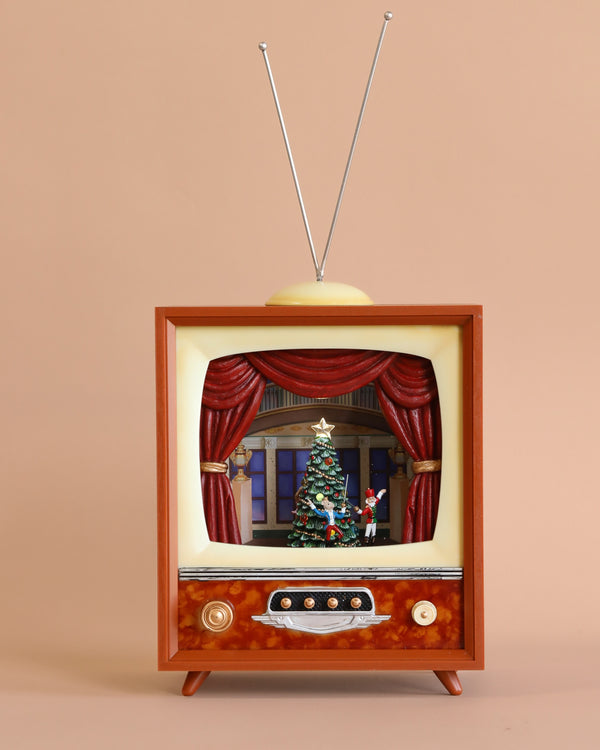 The Christmas Music TV With Nutcracker showcases a light-up scene of a decorated Christmas tree and presents, accompanied by softly playing Christmas melodies. This vintage set is designed with a wooden frame, large dials, and an antenna on top, all set against a simple beige background.