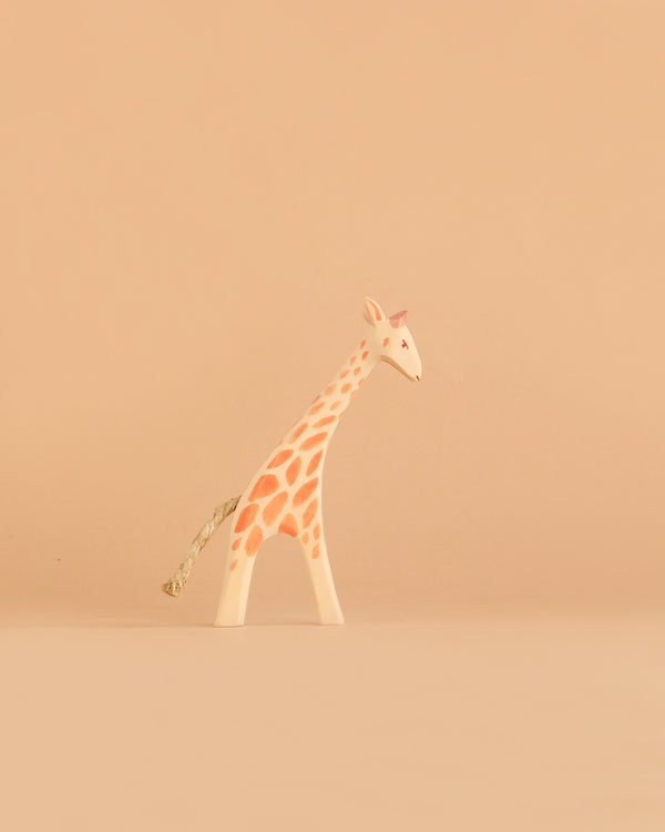 The Ostheimer Small Giraffe - Head Low, featuring orange spots and a rope tail, stands on a light beige background, exemplifying the charm of handcrafted toys.