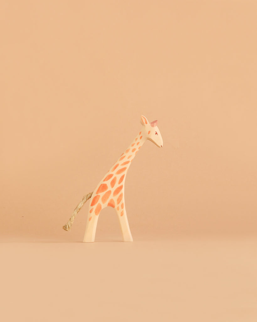 The Ostheimer Small Giraffe - Head Low, featuring orange spots and a rope tail, stands on a light beige background, exemplifying the charm of handcrafted toys.