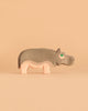 The Ostheimer Hippopotamus is a simple wooden toy featuring gray and pink colors, standing on a beige background. Handcrafted in the classic Ostheimer style, it has a green eye and minimal features, giving it a playful, minimalist appearance that encourages imaginative play.