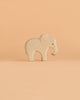 An elegant elephant figurine from the Ostheimer Handmade Wooden Safari Animals Set, inspired by traditional handcrafted wooden toys, stands on a simple peach-colored background.