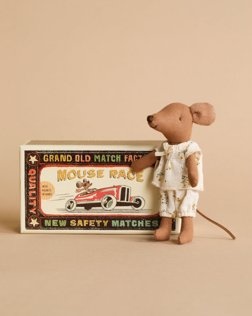 A Maileg Big Sister and Me Set mouse in patterned pajamas stands beside a vintage-style "Mouse Race" matchbox with a red race car illustration and decorative text on a beige background.