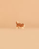 A small, brown and white dog figurine from the Ostheimer Handmade Wooden Dog Family Set, crafted from sustainably sourced wood in the signature Ostheimer style, stands on a plain beige background.