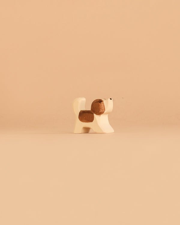A small, simple ceramic figurine of a brown and white dog stands alone on a light beige surface with a matching beige background, evoking the charm and warmth of handcrafted wooden toys that inspire imaginative play. Rewritten using product data: The Ostheimer Dog - Saint Bernhard, Small - Head Up stands alone on a light beige surface with a matching beige background, its handcrafted wooden form in brown and white bringing to mind the charm and warmth that inspires imaginative play.