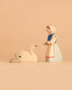 The Ostheimer Handmade Wooden Swan Girl Set features a beautifully handcrafted wooden figurine of a woman in a white dress and headscarf, standing before two wooden swans—one large and one small—set against a plain beige background. Inspired by classic Ostheimer toys and crafted from sustainably sourced materials, this set embodies timeless charm while reflecting care for the environment.