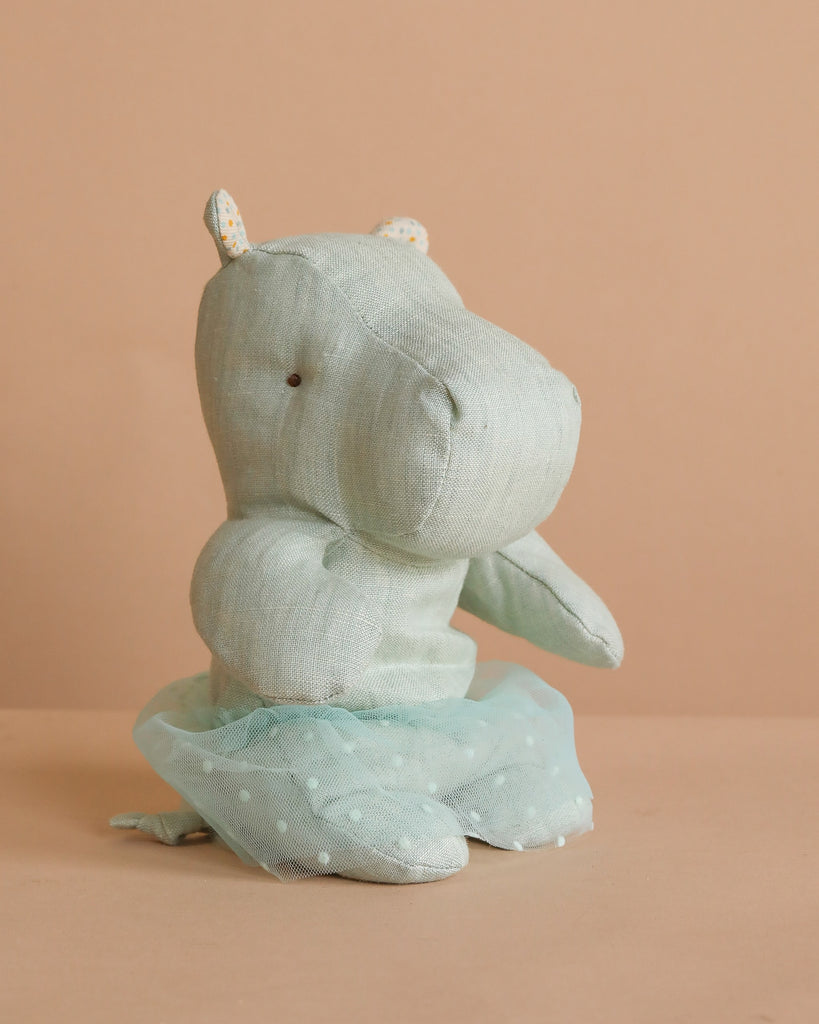 The Maileg Small Hippo With Skirt Stuffed Animal in mint sits upright on a beige surface, dressed in a sheer polka-dot tutu. Crafted from soft fabric, this adorable safari friend is shown against a matching beige background.