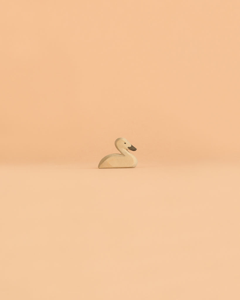 An Ostheimer Handmade Wooden Swan Girl Set, inspired by classic handcrafted wooden toys, is centered on a smooth, peach-colored background with plenty of empty space around it.