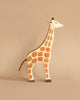 The Holztiger Handmade Wooden Safari Animals Set features a wooden giraffe toy with painted brown spots standing upright on a beige background, showcasing the charm of handcrafted wooden toys.