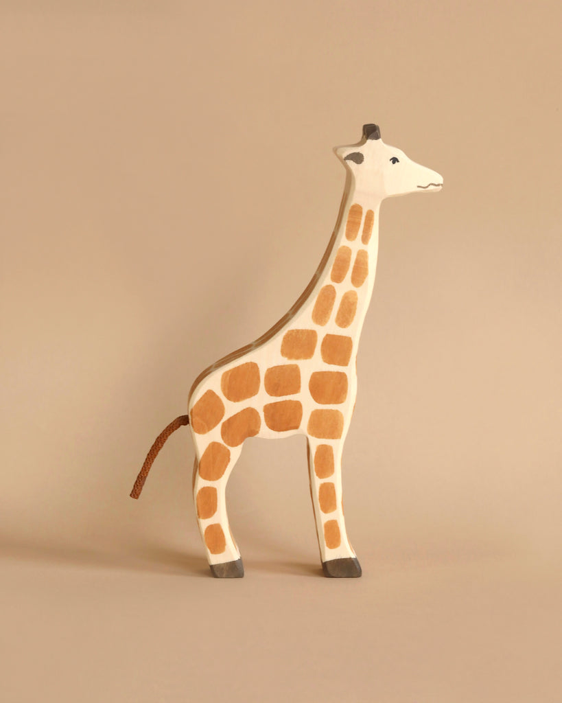 A handcrafted Holztiger Giraffe with a simple, minimalistic design stands on a neutral beige background. Made in Europe, the giraffe is painted with orange-brown spots and black hooves, and it has a small smile on its face, resembling the charming style of HOLZTIGER figures.