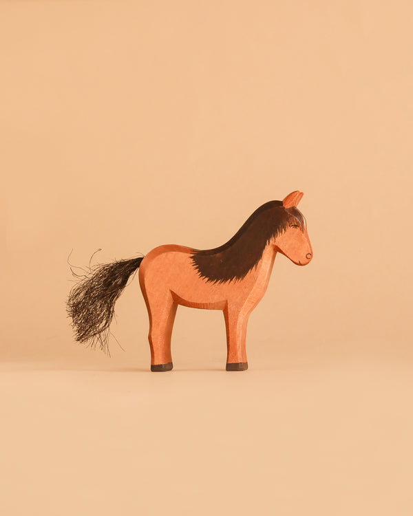 The Ostheimer Horse - Brown Colt, a handcrafted wooden toy horse with a black mane and tail, stands on a beige surface against a matching beige background, inviting imaginative play.
