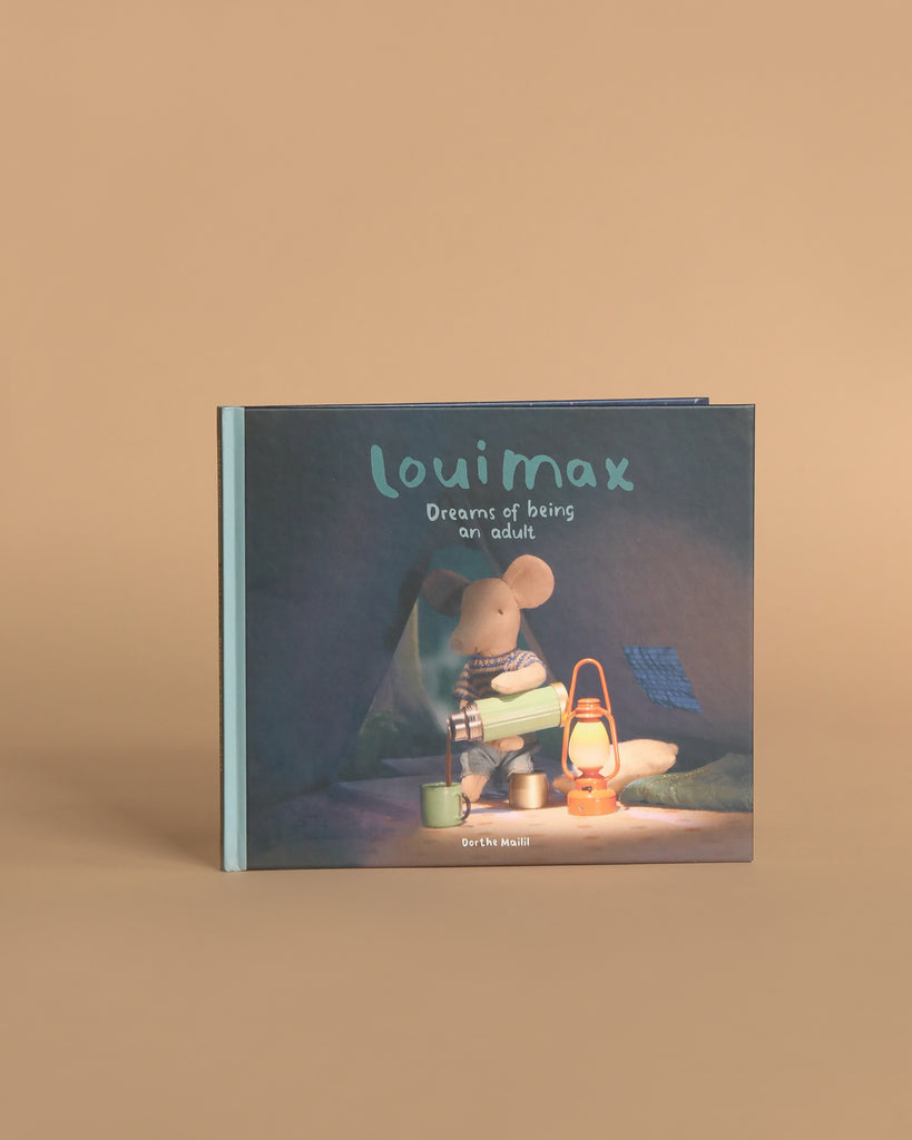 The Maileg LouiMax Little Explorer with Book Set features a Maileg mouse sitting beside two lanterns, including a Maileg lantern, inside a tent with a soft brown background, inspired by dreams of being an adult.