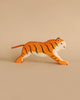 A handmade wooden tiger from the Holztiger Handmade Wooden Safari Animals Set, crafted from maple and beech with orange, black, and white markings, stands on a plain beige background.