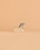 The Ostheimer Donkey - Resting, a small and minimalist wooden figurine with gray ears and mane, reminiscent of classic handcrafted toys, sits on a smooth, light peach background.