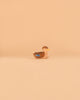 A small duck figurine from the Ostheimer Handmade Wooden Farm Animals Set, handcrafted from sustainably sourced wood and featuring brown, tan, and blue details, is centered on a plain beige background.