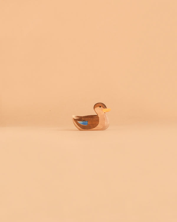 The Ostheimer Duck, Swimming is a small handcrafted wooden duck figurine with brown, white, and blue markings, resting on a plain beige background. Inspired by the quality craftsmanship of Ostheimer toys, this delightful piece exemplifies non-toxic toys made with care and attention to detail.