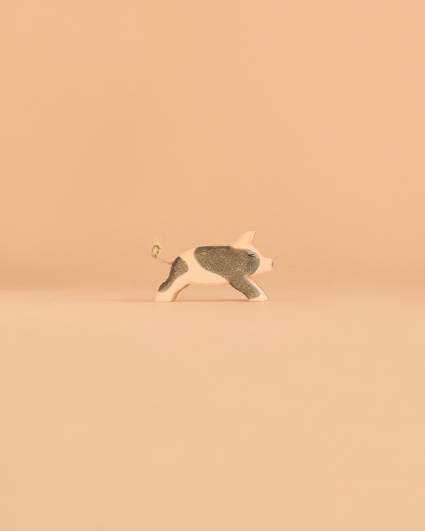 The Ostheimer Spotted Piglet - Running figurine, with its charming pink and black design, stands on a plain beige background.