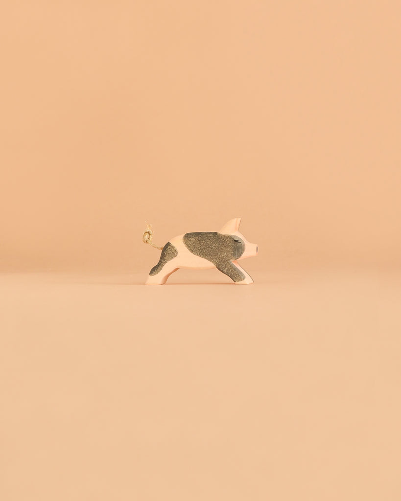 A handcrafted pig figurine with black spots and a curled tail from the Ostheimer Handmade Wooden Farm Animals Set, made from sustainably sourced materials in the distinctive Ostheimer style, is displayed against a plain beige background.