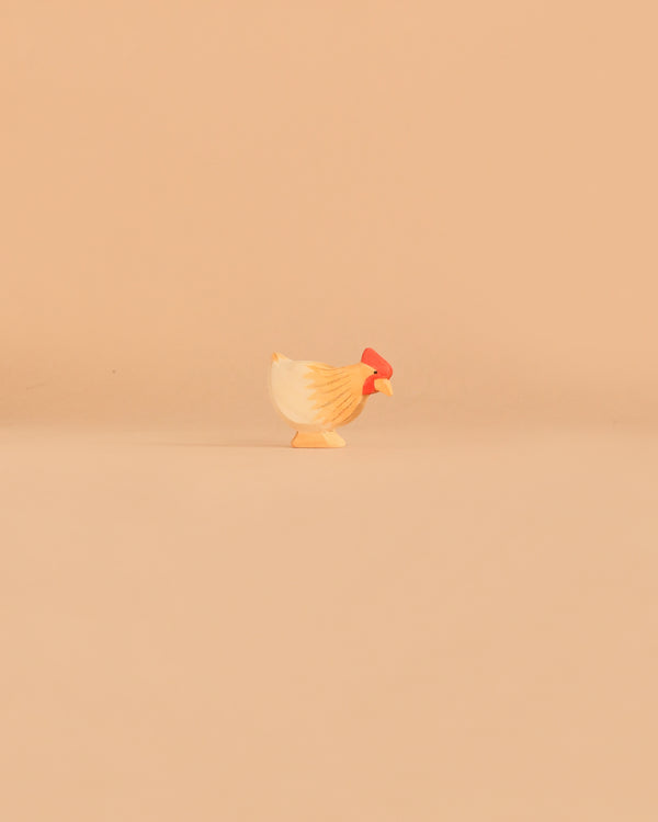 The Ostheimer Hen Standing - Ochre, a small handcrafted wooden figurine featuring a red comb, is centered against a plain light tan background, evoking the classic style of Ostheimer toys and crafted from sustainably sourced materials.