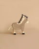 A charming figure from the Holztiger Handmade Wooden Farm Animals Set, this wooden zebra features painted black and white stripes, a black mane, and a white rope tail, displayed on a plain beige background.