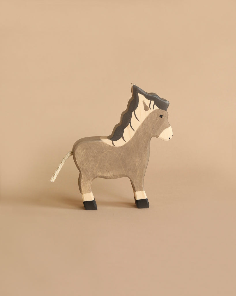 A charming figure from the Holztiger Handmade Wooden Farm Animals Set, this wooden zebra features painted black and white stripes, a black mane, and a white rope tail, displayed on a plain beige background.