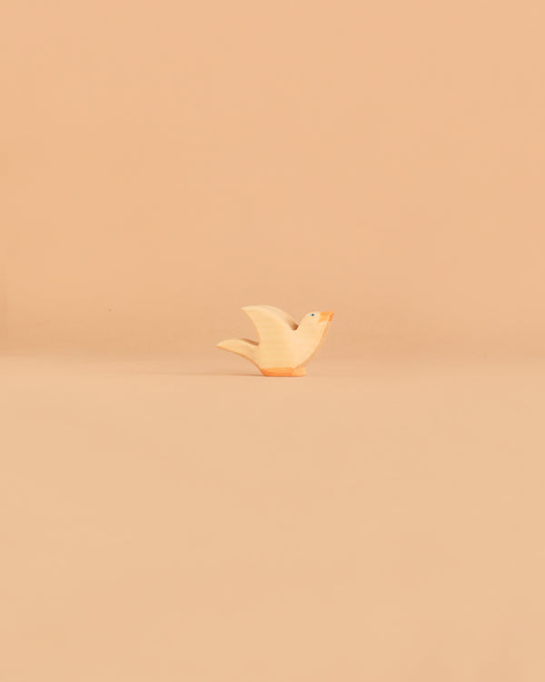 A small, white Ostheimer Bird - Flying Dove figurine with an orange beak stands on a pale beige surface against a matching plain background, reminiscent of the charming handcrafted quality and non-toxic materials for which Ostheimer wooden toys are beloved.