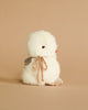 A fluffy white stuffed animal resembling an Easter Basket Set baby chick with a peach ribbon around its neck, set against a smooth beige background.