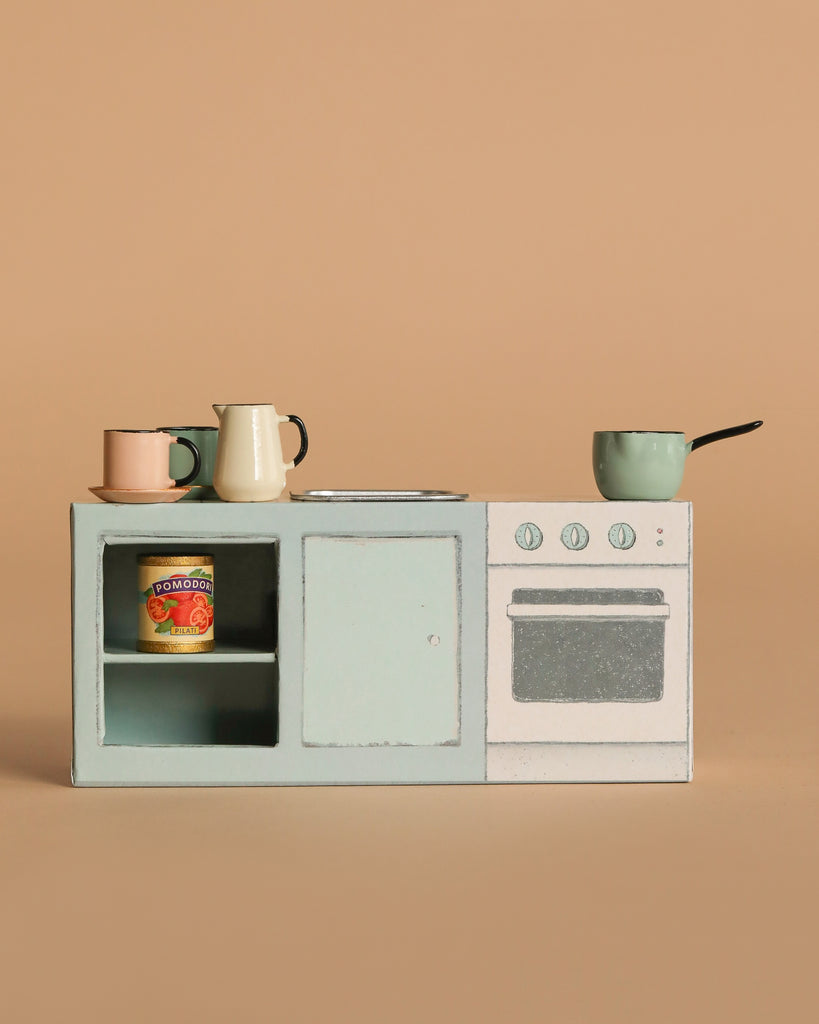 The Maileg On The Go Suitcase Set features a miniature toy kitchen in mouse size with a stove, oven, shelves, tiny pots, cups, and a can of pomodoro tomatoes, all displayed against a plain beige background.