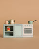 The Maileg Kitchen Counter, Mouse Size, features pastel cookware, a can of tomatoes on the shelf, a stove, and a sink—all set on a compact counter against a plain beige background.