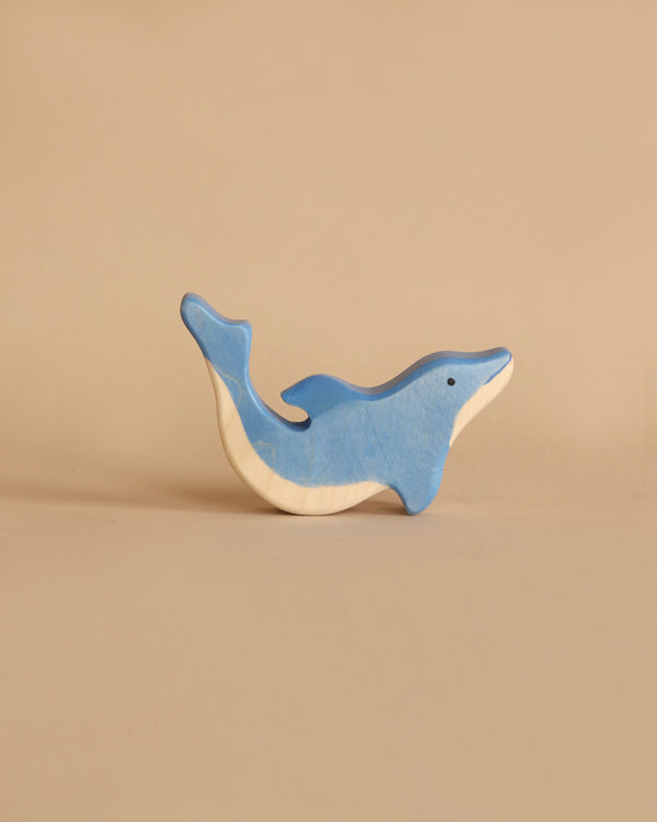 A wooden toy dolphin, handcrafted from high-quality wood and painted blue with a natural wood-colored underbelly, is shown against a beige background. The Holztiger Dolphin, Small, part of the renowned HOLZTIGER figures made in Europe, is positioned as if swimming upwards.