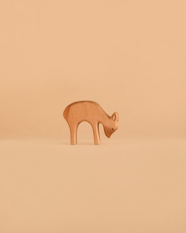 An Ostheimer Deer - Eating figurine stands on a plain, light brown surface with a matching beige background, exemplifying the timeless charm and handcrafted sustainability of Ostheimer wooden toys.