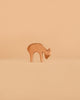 An Ostheimer Deer - Eating figurine stands on a plain, light brown surface with a matching beige background, exemplifying the timeless charm and handcrafted sustainability of Ostheimer wooden toys.