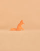 An Ostheimer Handmade Wooden Woodland Animals fox figurine rests on a neutral beige background, turned to the right. Its simple, smooth form in warm orange highlights the artisanal charm and sustainable craftsmanship typical of Ostheimer’s timeless wooden toys.
