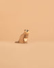 A small, carved wooden raccoon figurine from the Ostheimer Handmade Wooden Woodland Animals Set sits on a smooth beige surface with a matching beige background, reminiscent of handcrafted toys.