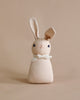 A Polka Dot Club Rabbit Rattle - Peach with long ears and embroidered eyes and nose, wearing an organic cream necktie around its neck, set against a plain beige background.