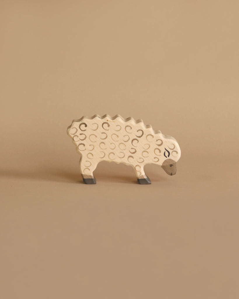 A small wooden toy resembling a sheep, handcrafted wood and painted beige with darker curved lines representing wool texture. The high-quality Holztiger Sheep, Eating stands on a neutral beige background, and its simple design includes a gray snout and feet, reminiscent of HOLZTIGER figures.