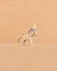 The Ostheimer Donkey - Small is a minimalist wooden figurine inspired by classic Ostheimer designs, featuring painted gray details and a simple rope tail. It stands on a beige surface with a plain beige background—ideal for imaginative play and collectors of handcrafted wooden toys.