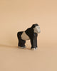 A small Holztiger Handmade Wooden Safari Animals Set gorilla figurine, crafted from maple and beech wood and painted black and beige, stands on a plain beige surface against a matching background.