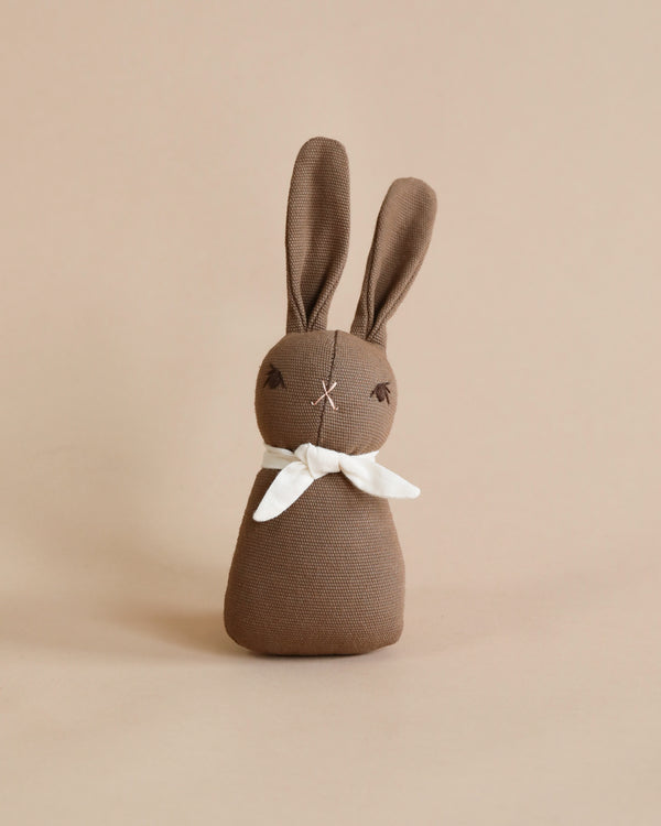 A Polka Dot Club Rabbit Rattle - Brown with long ears and embroidered eyes, wearing an organic cream necktie, stands upright against a plain beige background.