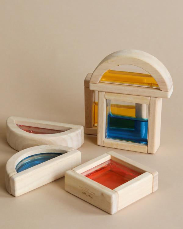 Four Wooden Water Blocks with colorful, translucent acrylic centers in shapes of arches and rectangles, arranged on a beige surface.